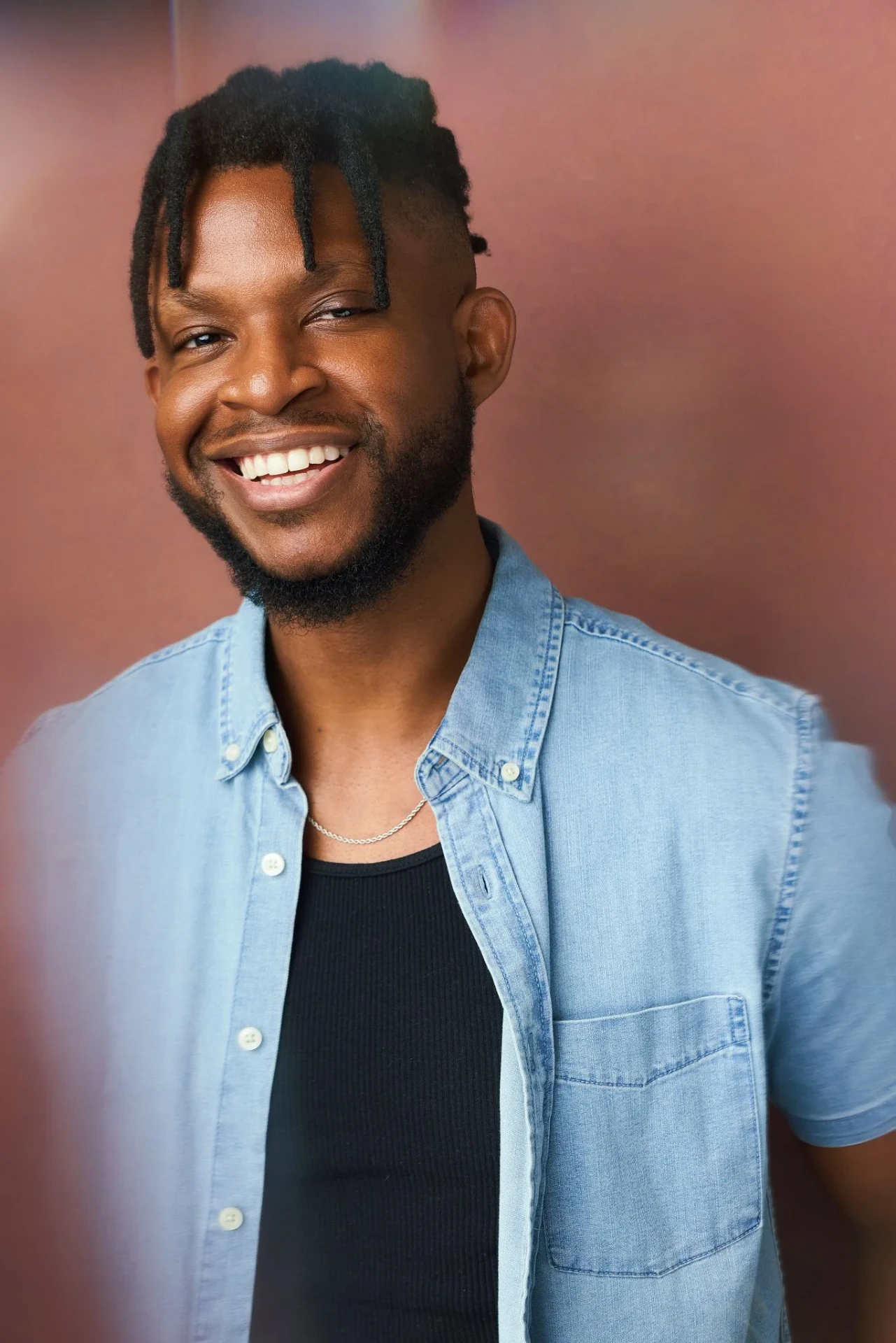 Editorial actor headshot of smiling actor in a denim shirt on a mauve backdrop, photographed by an Atlanta actor headshot photographer
