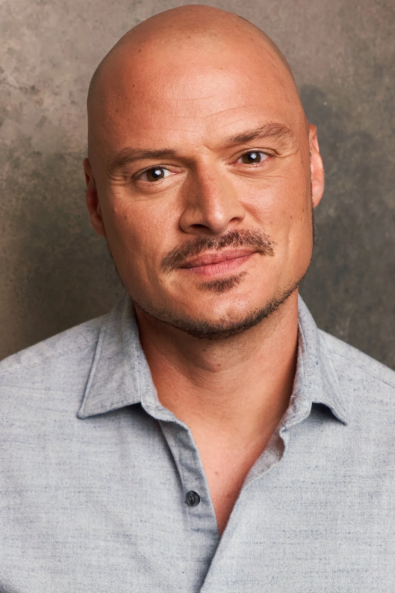 Editorial actor headshot of bald actor in a gray shirt on a textured backdrop, photographed by an Atlanta actor headshot photographer