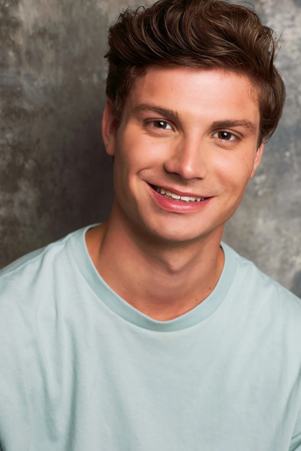 Editorial actor headshot of smiling actor in a mint tee on a gray backdrop, photographed by an Atlanta actor headshot photographer