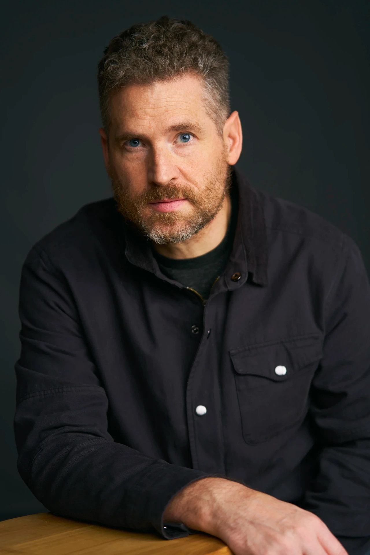 Editorial actor headshot of bearded actor in a black jacket on a dark backdrop, photographed by an Atlanta actor headshot photographer