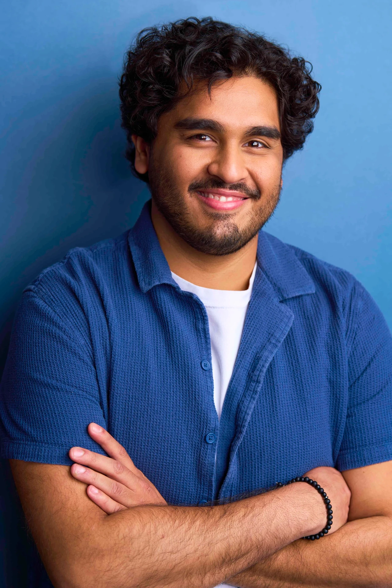 Smiling male actor headshot in a blue shirt with arms crossed in Atlanta
