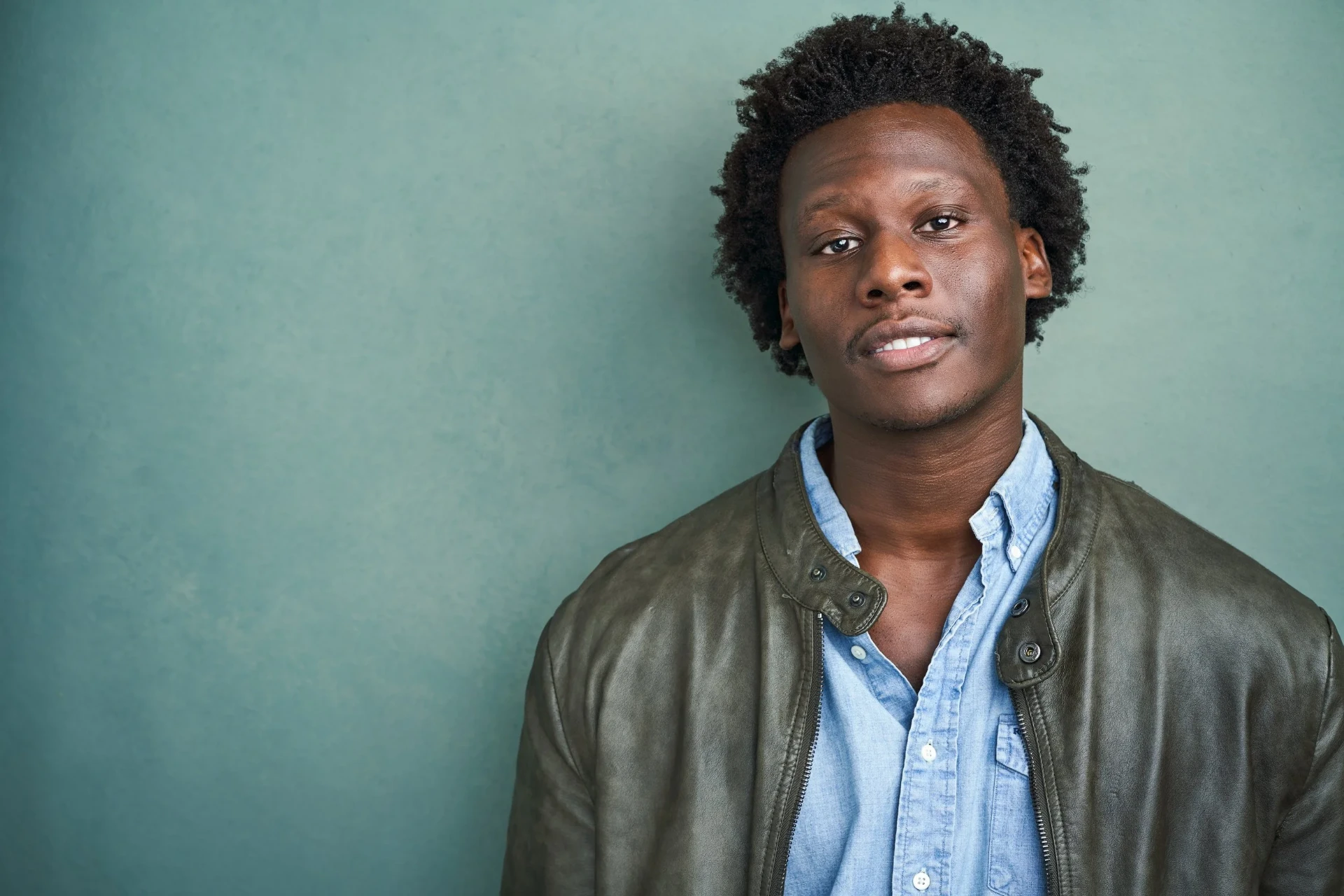 Editorial actor headshot of actor in a leather jacket on a teal backdrop, photographed by an Atlanta actor headshot photographer