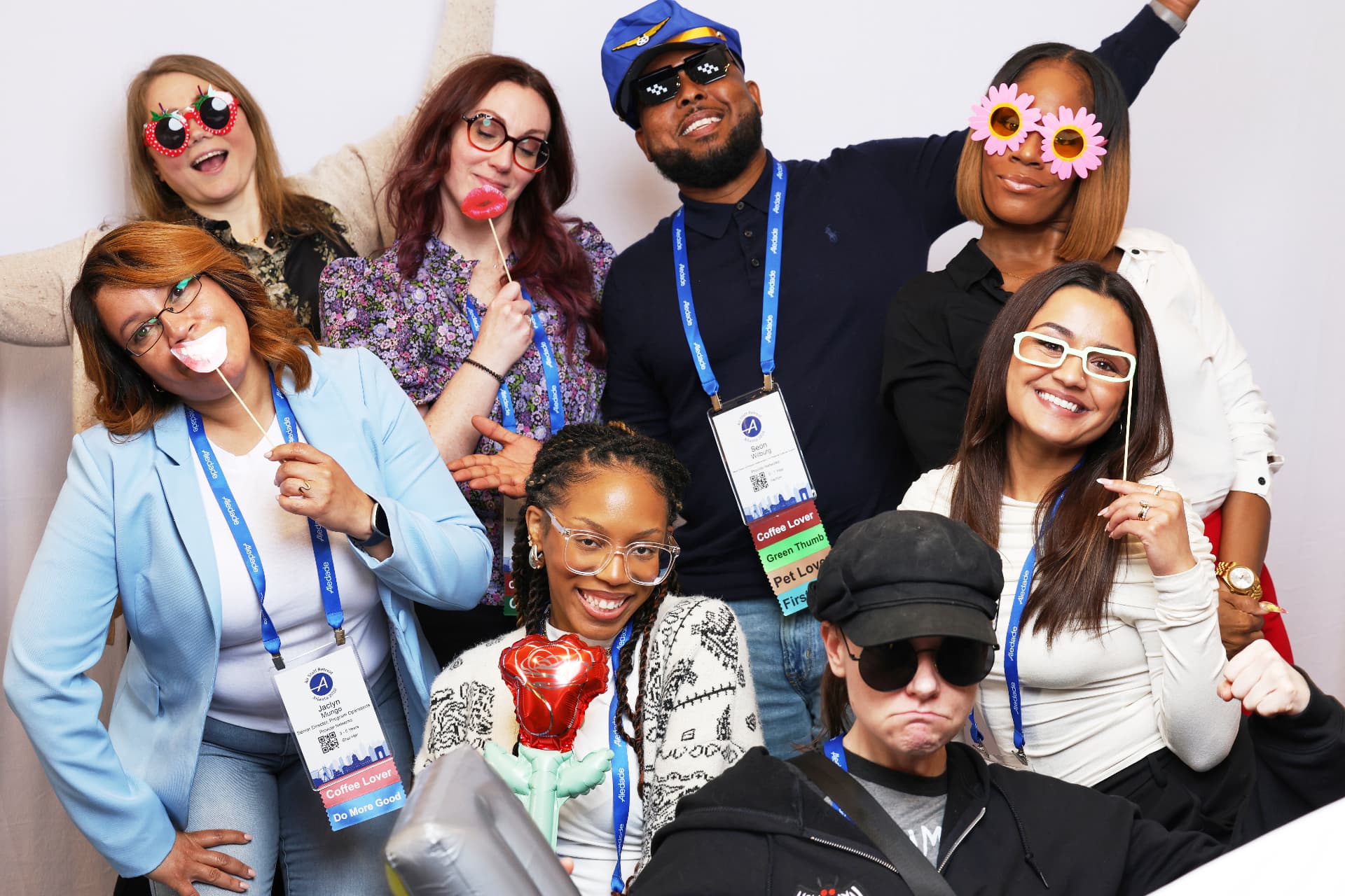 Eight Aledade attendees making playful faces with novelty glasses and props at an Atlanta event photobooth