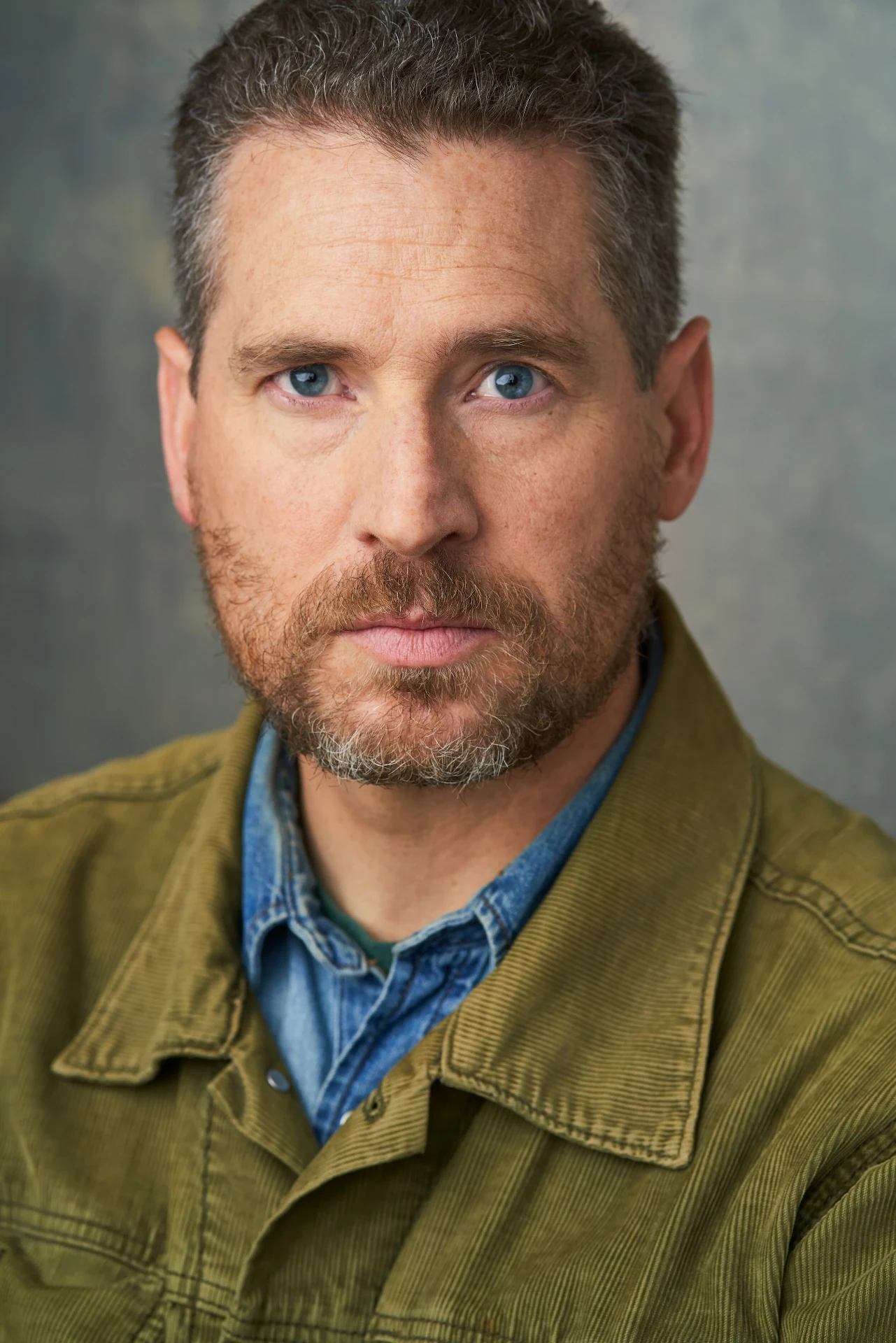 Editorial actor headshot of actor in an olive jacket on a gray backdrop, photographed by an Atlanta actor headshot photographer
