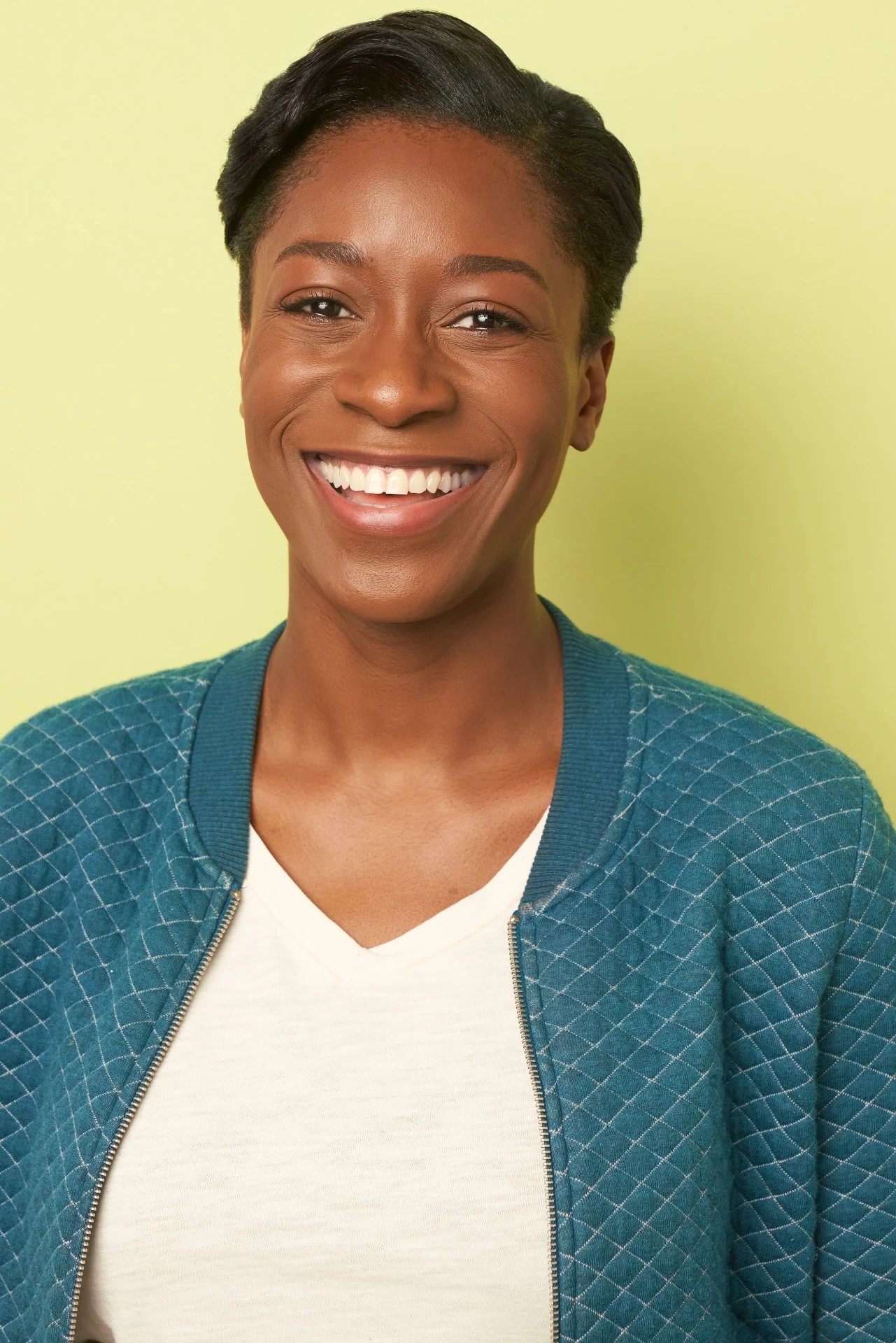 Smiling actress headshot in a teal cardigan on a yellow backdrop in Atlanta