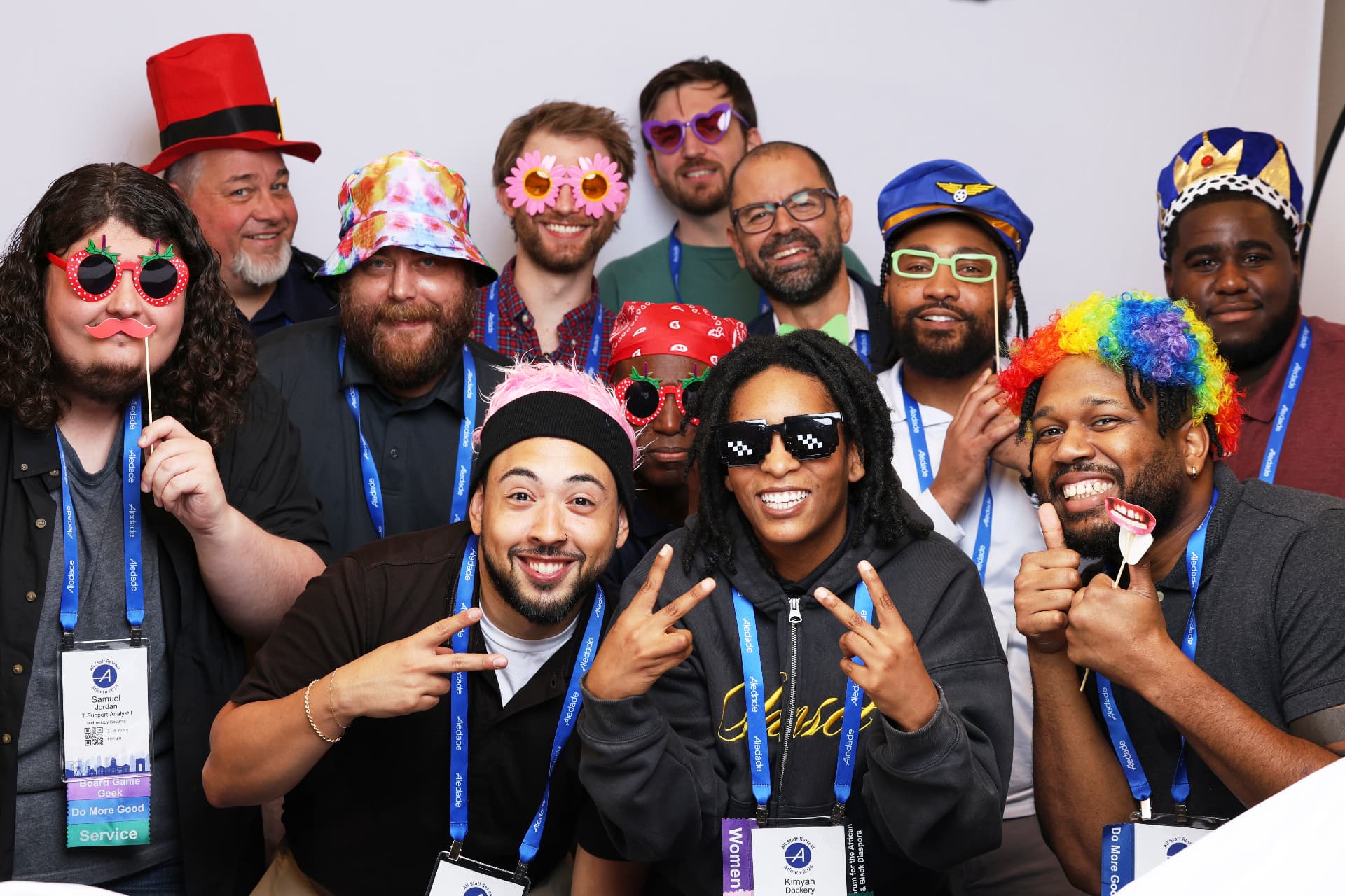 Twelve Aledade conference attendees posing with party hats and novelty props at an Atlanta event photobooth