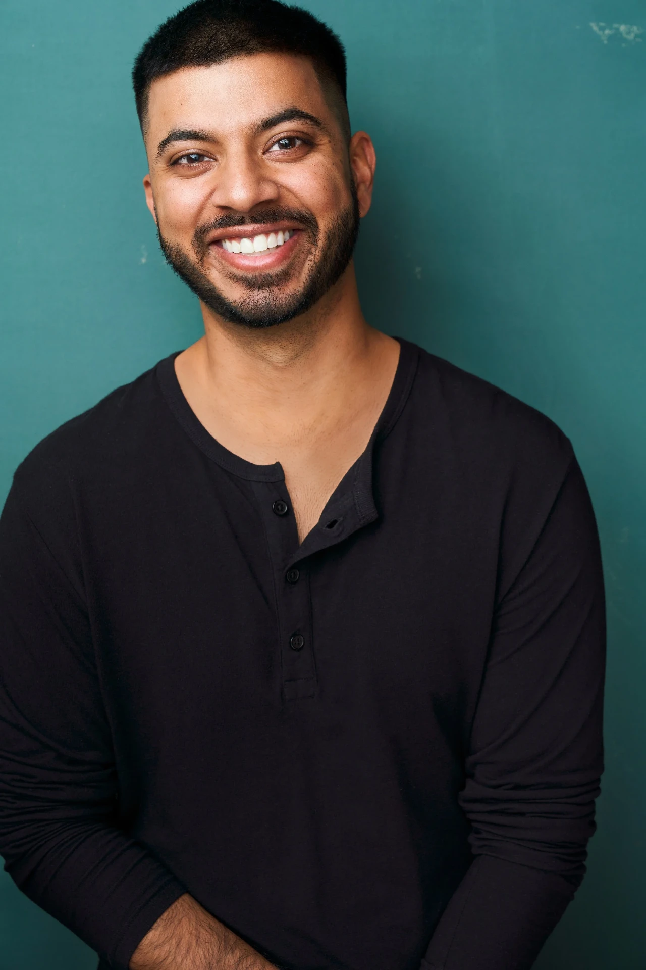 Editorial actor headshot of smiling actor in a black henley on a teal backdrop, photographed by an Atlanta actor headshot photographer