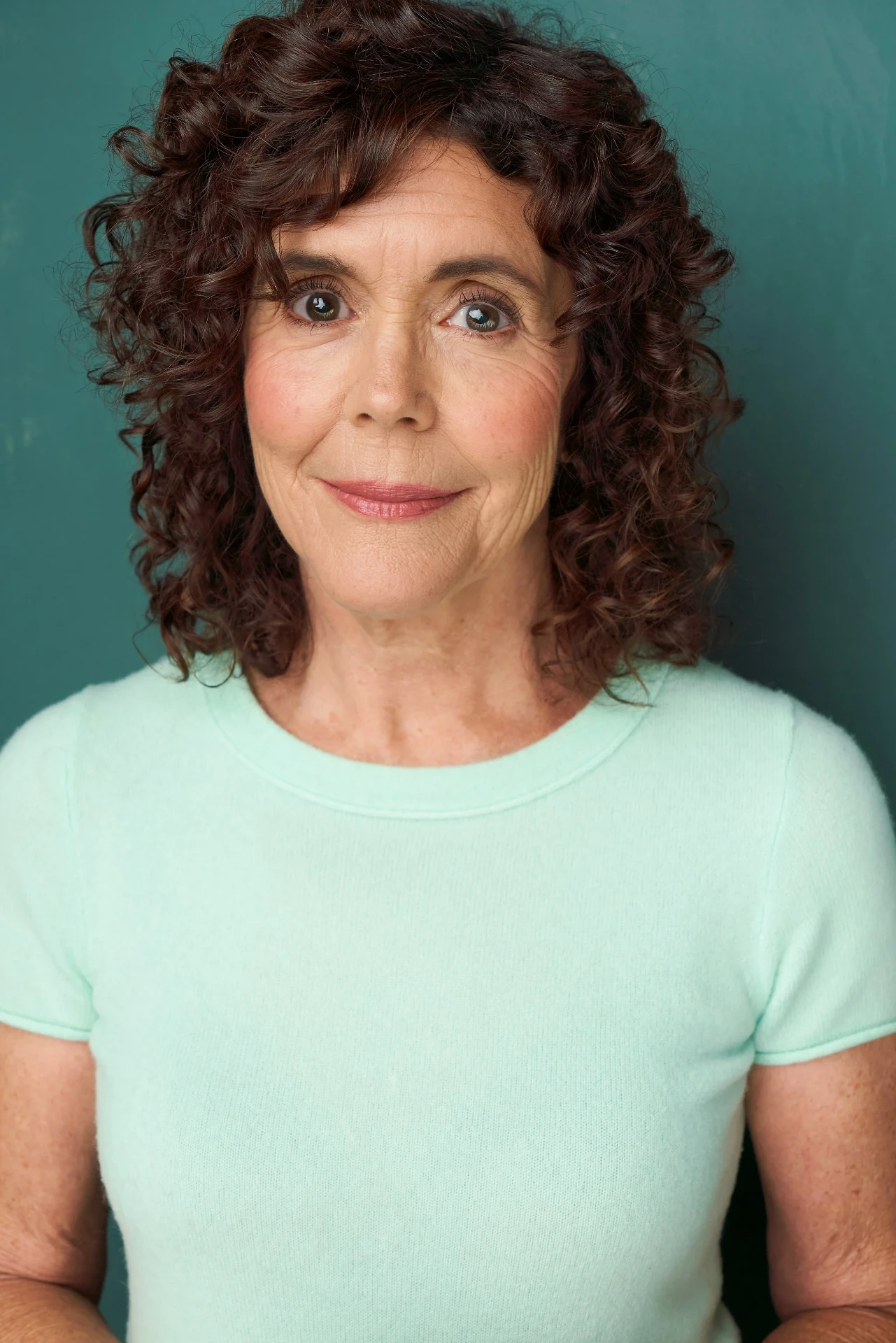 Editorial actor headshot of curly-haired actress in a mint tee on a teal backdrop, photographed by an Atlanta actor headshot photographer