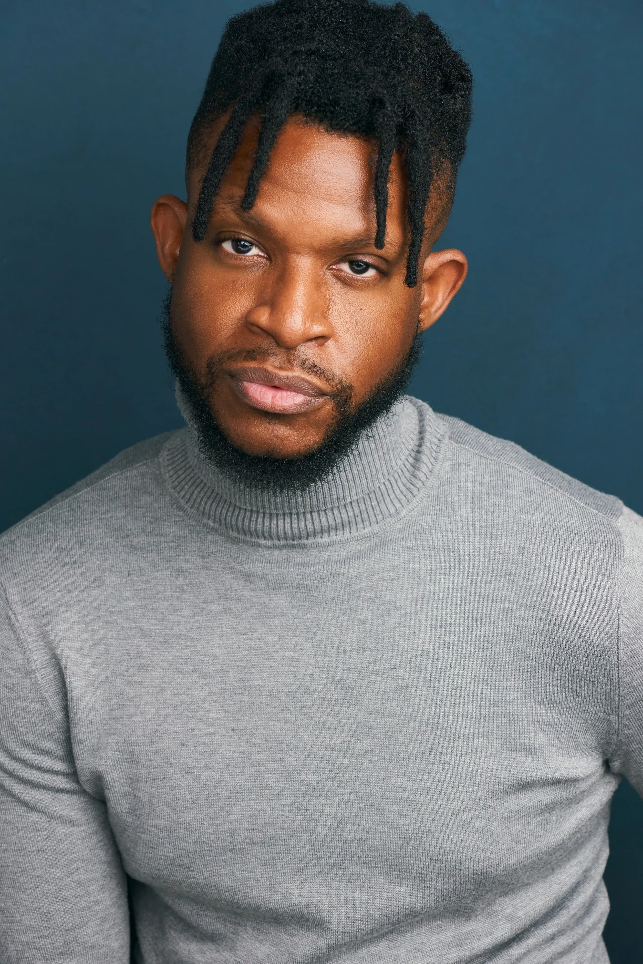 Editorial actor headshot of actor in a gray turtleneck on a blue backdrop, photographed by an Atlanta actor headshot photographer