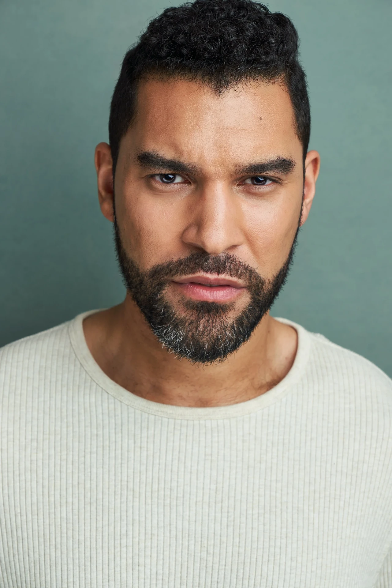 Editorial actor headshot of bearded actor in a cream sweater on a teal backdrop, photographed by an Atlanta actor headshot photographer